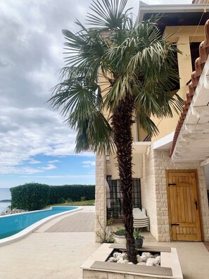 A building with a palm tree, a pool, and a view of the sea. - Villa Provence Budva (Budva)
