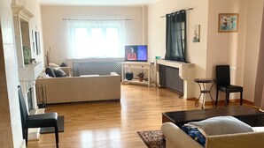 Uma sala de estar com televisão, sofá, poltronas, piso de madeira e lareira.
