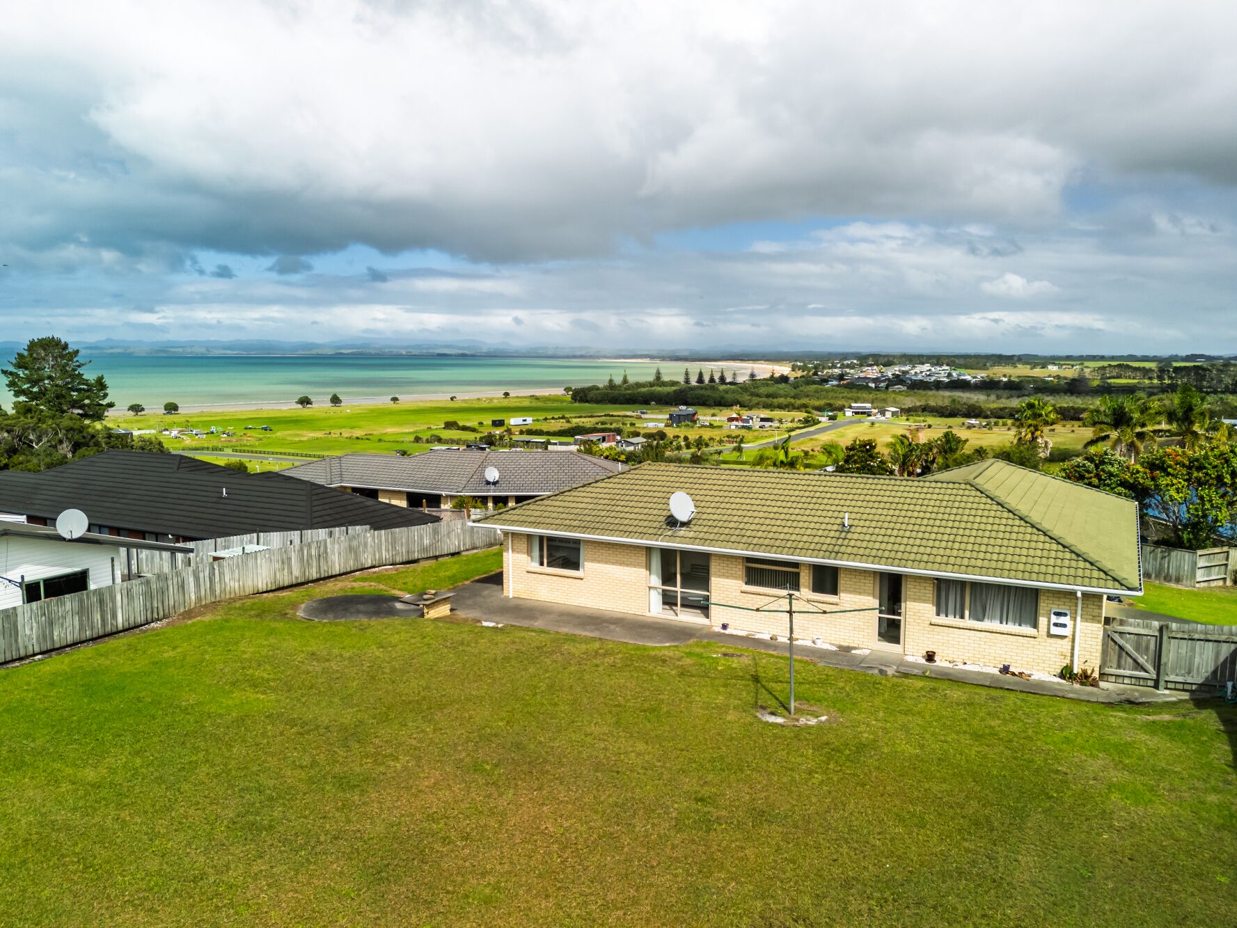 Un quartier résidentiel avec des maisons, une pelouse et une vue sur une plage et l’océan.