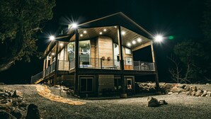 A two-story wooden cabin with a balcony, surrounded by trees and a gravel path.