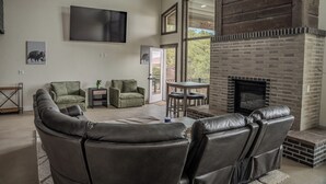 A modern living room with leather sofas, a fireplace, and a large TV mounted on the wall.