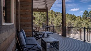 A wooden deck with outdoor seating, a table, and a view of trees.