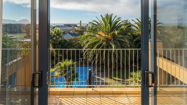 Ein Balkon mit Blick auf einen Swimmingpool, Palmen und Gebäude in der Ferne.