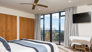 Ein Schlafzimmer mit einem großen Bett, einem Deckenventilator, einem Fernseher und einem Balkon mit Blick.