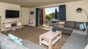 Ein modernes Wohnzimmer mit Flachbildfernseher, Couchtisch, Sofa und einer Essecke mit Tisch und Stühlen.