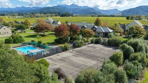 Un quartier résidentiel avec des maisons, une piscine et un court de tennis, le tout entouré de verdure et de montagnes.