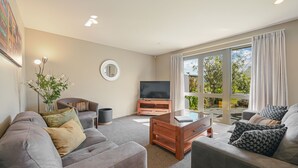 Un salon moderne avec un canapé, une table basse, un téléviseur et une grande fenêtre avec des rideaux.