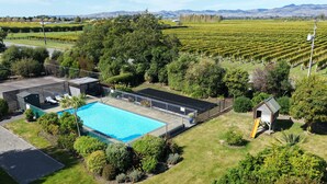 Un espace piscine doté d’une terrasse entourée d’une clôture, d’un petit abri de jardin et d’un bâtiment avec un toit en pente.