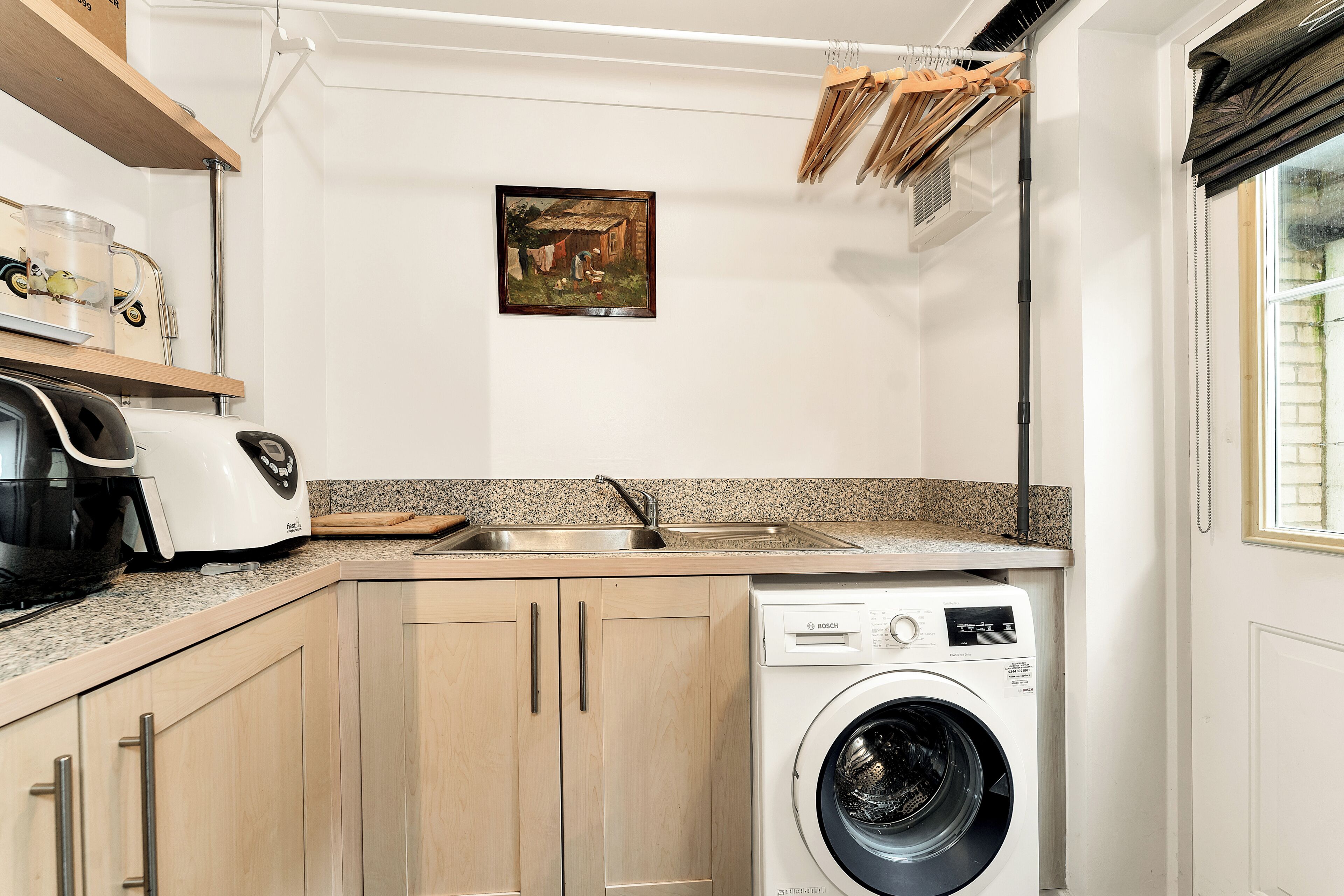 A compact kitchen with a Bosch washing machine, a coffee maker, and a small sink.