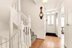 A staircase with white balusters, a wooden floor, a wall-mounted clock, and a door with a frosted glass panel. - Spacious 3BR Home w/ Private Garden & Parking (Cambridge)