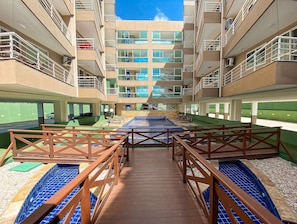 A multi-level hotel with a central swimming pool, outdoor seating, and a covered walkway. - Lindo Apto no Cumbuco por Be My Guest (Caucaia)