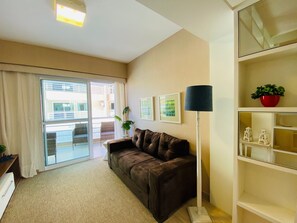 Ein Wohnzimmer mit braunem Sofa, einer Stehlampe, einem Blumentopf und einer Schiebetür zu einem Außenbereich.