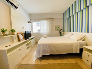Una habitación de hotel con cama, televisor, escritorio y ventana con cortinas.