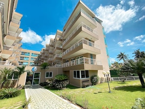 A multi-story hotel with balconies, a paved entrance, and a well-maintained lawn. - Lindo Apto no Cumbuco por Be My Guest (Caucaia)
