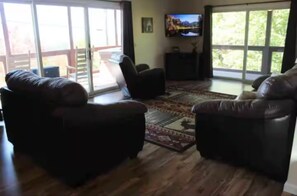 A living room with two leather sofas, a television on the wall, and a large window. - The Graceful Retreat: Secluded Cabin w/ Hot Tub (Sevierville)