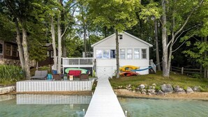 A house with a dock leading to a clear water body, surrounded by trees.