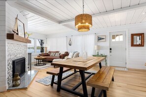A spacious living room with a fireplace, a dining table, and a large window overlooking a body of water. - Firefly Cottages on Bass Lake | Sandy Frontage, Dock, Kayaks, Near Downtown TC (Traverse City)
