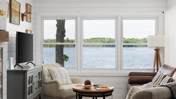 A room with a large window overlooking a body of water, a television, a fireplace, and a cozy seating area.