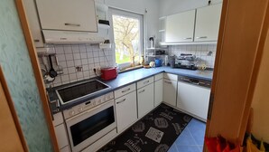 Eine Küche mit weißen Schränken, einem Bosch-Ofen, einem roten Toaster und einem Fenster mit Blick auf Bäume.