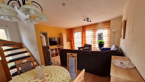 Ein Wohnzimmer mit einer Couch, einem Fernseher, einer Holztreppe und einem Essbereich mit einem Tisch.