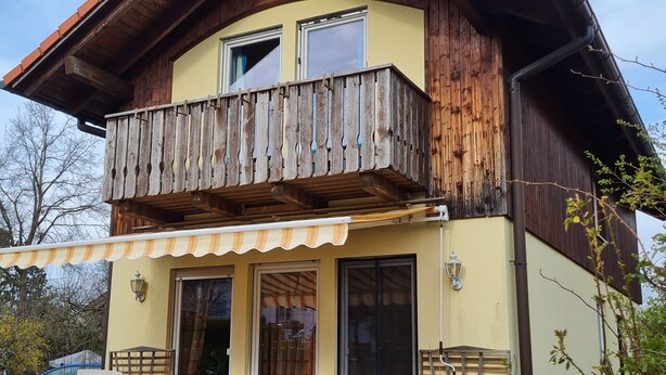 Ein zweistöckiges Holzhaus mit Balkon, Terrasse und Garten.