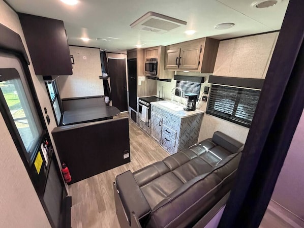 A compact RV interior with a kitchenette, a seating area, and a small dining table.