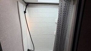 A compact bathroom with a shower, toilet, and a small window above the shower. - Rivers Edge RV Stay at Myakka Cove (Venice)