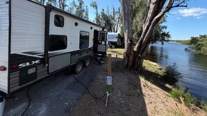 A recreational vehicle (RV) parked by a lake with trees in the background. - Rivers Edge RV Stay at Myakka Cove (Venice)