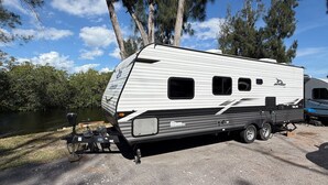 A white RV with a side-mounted awning, a small enclosed rear compartment, and a front hitch. - Rivers Edge RV Stay at Myakka Cove (Venice)
