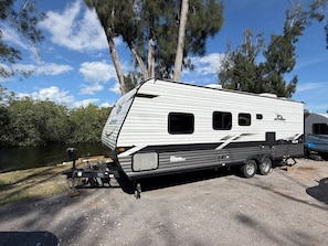 Een witte camper met een uitklapbare luifel aan de zijkant, een klein opbergruimte achterin en een trekhaak aan de voorkant.