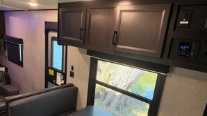 A compact RV interior with a dining area, a window with a view of a rocky landscape, and built-in cabinets. - Rivers Edge RV Stay at Myakka Cove (Venice)