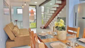 A dining area with a wooden table set for four, a sofa, and a staircase in the background. - Bella Arte Porto das Dunas (Aquiraz)