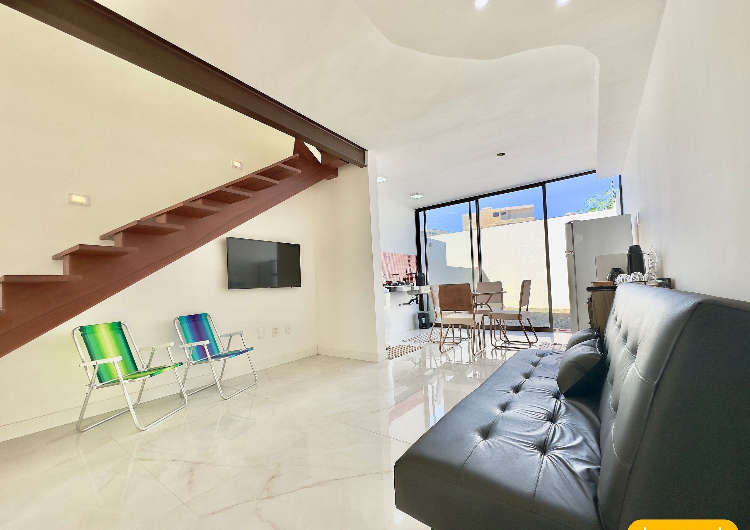 A modern living room with a staircase, a flat-screen TV, a sofa, and a dining area with chairs.
