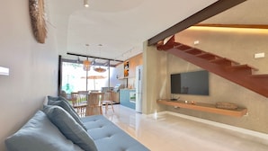 A modern living room with a sofa, dining area, kitchen, and staircase. - Bella Arte Porto das Dunas (Aquiraz)