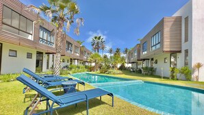 A modern hotel with a swimming pool, lounge chairs, and palm trees. - Bella Arte Porto das Dunas (Aquiraz)