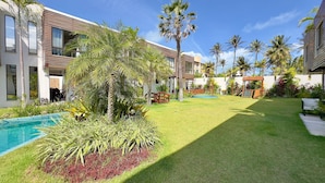 A modern hotel with a swimming pool, lush greenery, and a clear blue sky. - Bella Arte Porto das Dunas (Aquiraz)