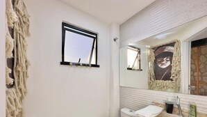 Un baño con espejo, toalla, lavamanos y ventana.