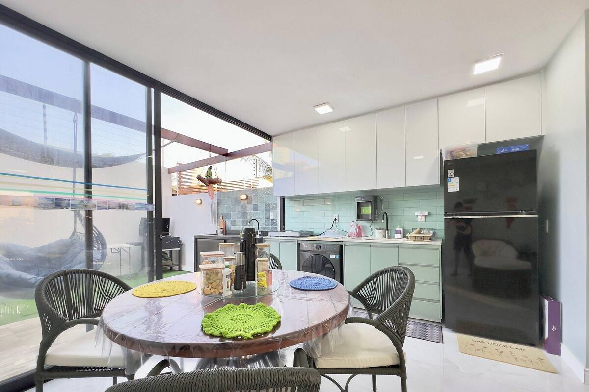 A modern kitchen with a dining area, large windows, and a refrigerator.