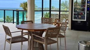 A balcony with a table and chairs, a vending machine, and a view of the ocean. - Vila Porto Beira Mar - VSH (Ipojuca)