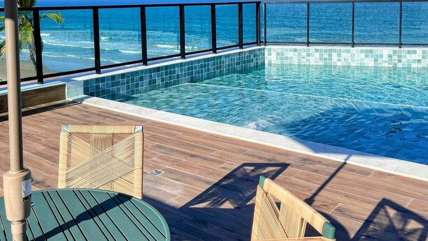 An infinity pool with a view of the ocean, wooden deck, and two wicker chairs. - Vila Porto Beira Mar - VSH (Ipojuca)