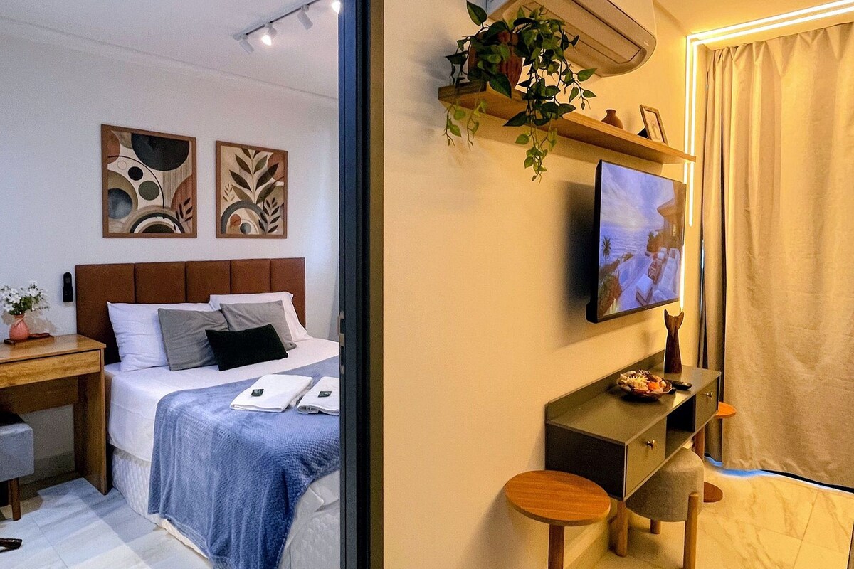 A hotel room with a bed, a desk, a TV, and a small plant.