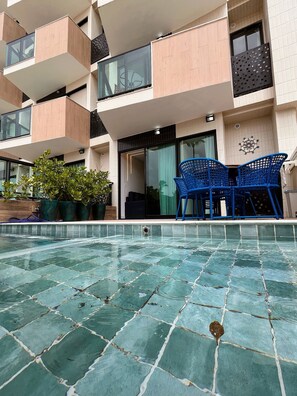 A modern building with a swimming pool, blue chairs, and potted plants. - Vila Porto Beira Mar - VSH (Ipojuca)