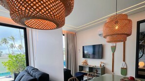 A modern dining area with a glass table, woven pendant lights, and a view of palm trees outside. - Vila Porto Beira Mar - VSH (Ipojuca)