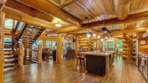 L’intérieur d’une cabane en rondins, avec un escalier en bois, un coin cuisine et un espace repas.