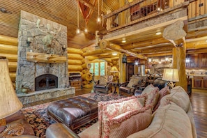 A log cabin interior with a stone fireplace, leather furniture, and a rustic wooden ceiling. - Laurelwood Lodge Theater Hot Tub 5BR Family Games (Ranger)