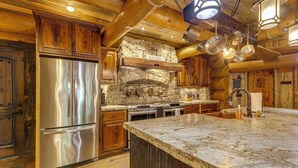 Une cuisine dotée de meubles en bois, d’une cheminée en pierre, d’appareils électroménagers en acier inoxydable et d’un plan de travail en granit.