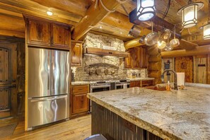A kitchen with wooden cabinets, a stone fireplace, stainless steel appliances, and a granite countertop. - Laurelwood Lodge Theater Hot Tub 5BR Family Games (Ranger)