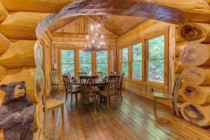 A log cabin interior with a dining table, chairs, a chandelier, and large windows. - Laurelwood Lodge Theater Hot Tub 5BR Family Games (Ranger)