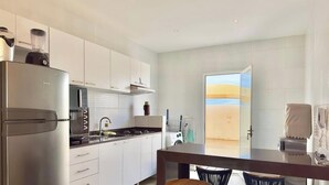 Una cocina moderna con refrigerador, estufa y lavavajillas, un comedor con mesa y sillas, y un amplio ventanal con vistas a un paisaje desértico.