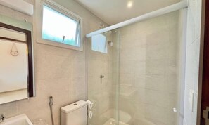 A modern bathroom with a glass shower enclosure, a toilet, a sink, and a window providing natural light. - Boas Vistas - Canoa Quebrada (Aracati)